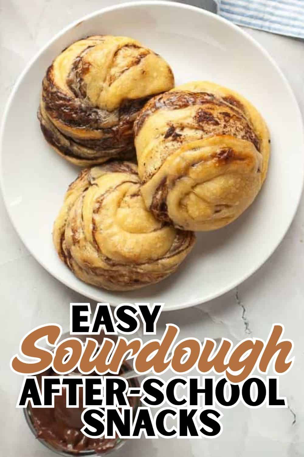 Freshly baked sourdough rolls with chocolate swirls on a white plate.