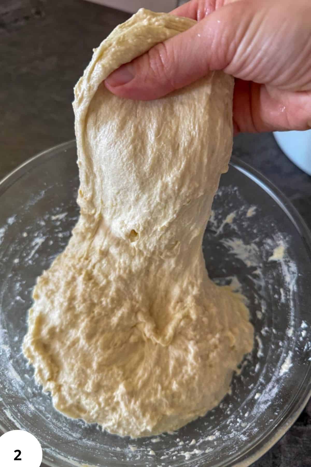 Hand performing stretch and fold technique for sourdough bread dough.