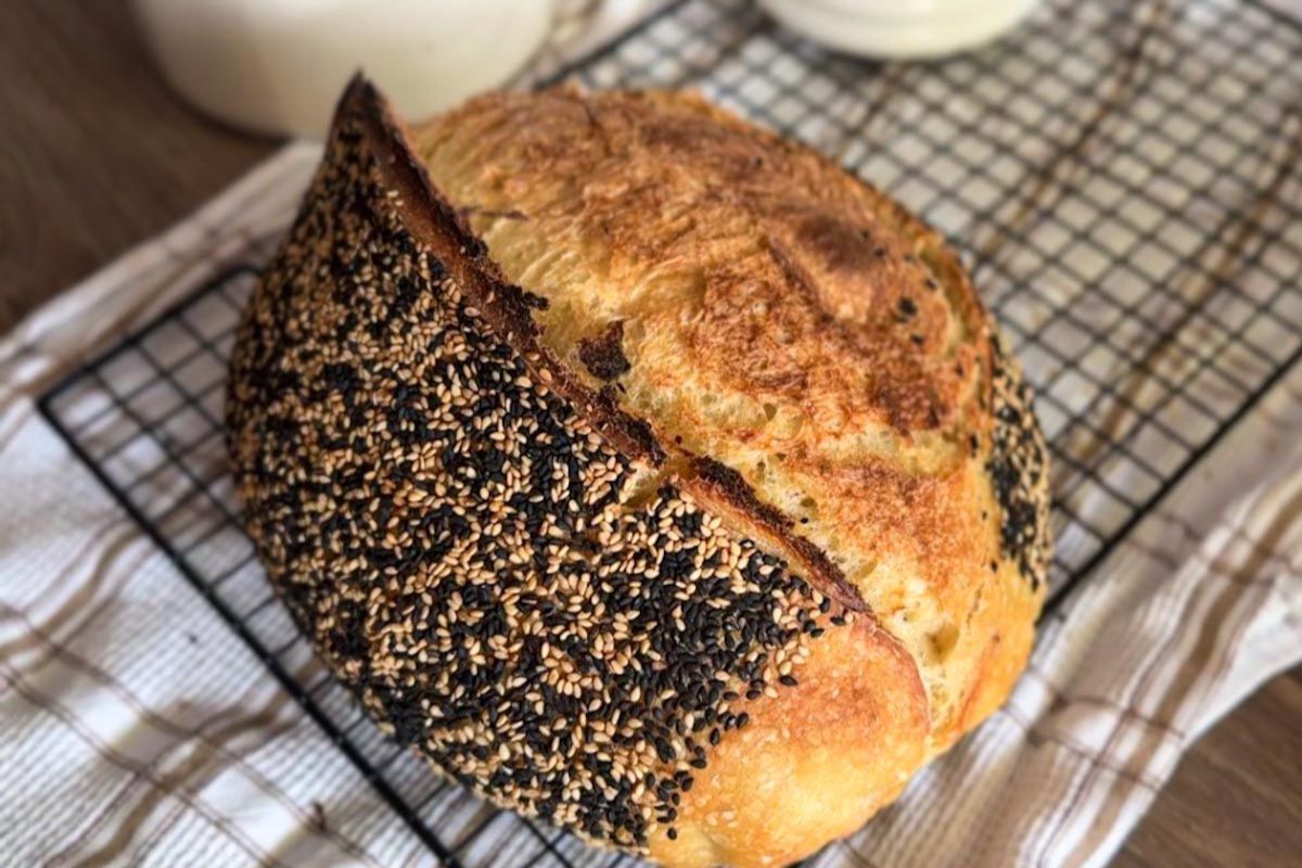Freshly baked sourdough bread with sesame seed crust on cooling rack.