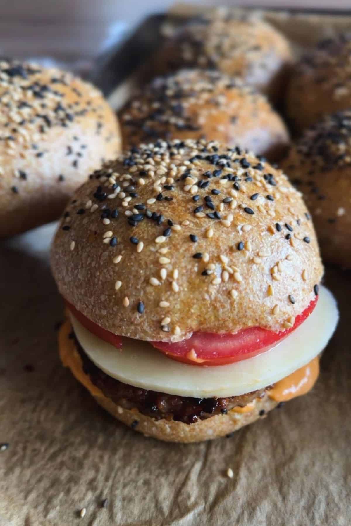 Freshly baked burger bun with sesame and poppy seeds, topped with fresh tomato, onion, and cheese.