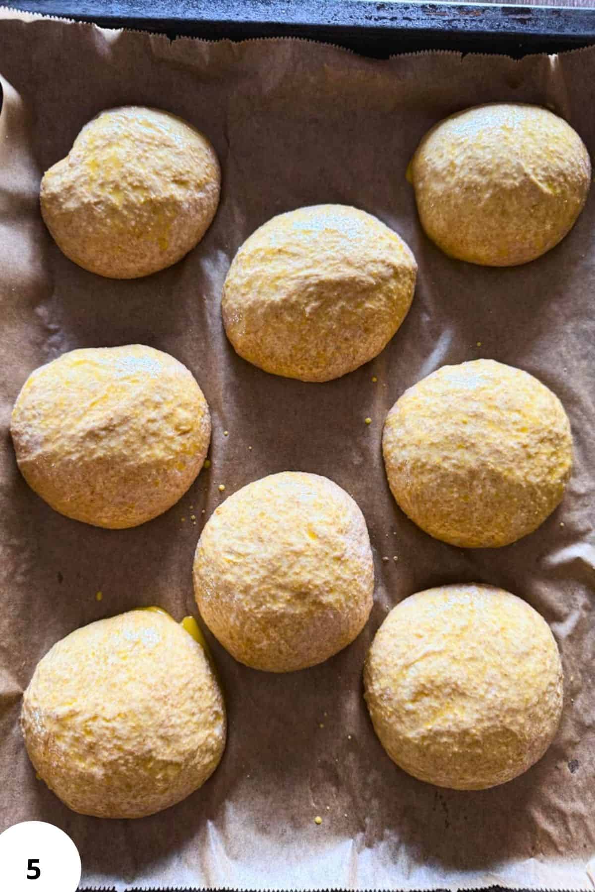 Freshly baked bread rolls coated with flour on baking sheet.