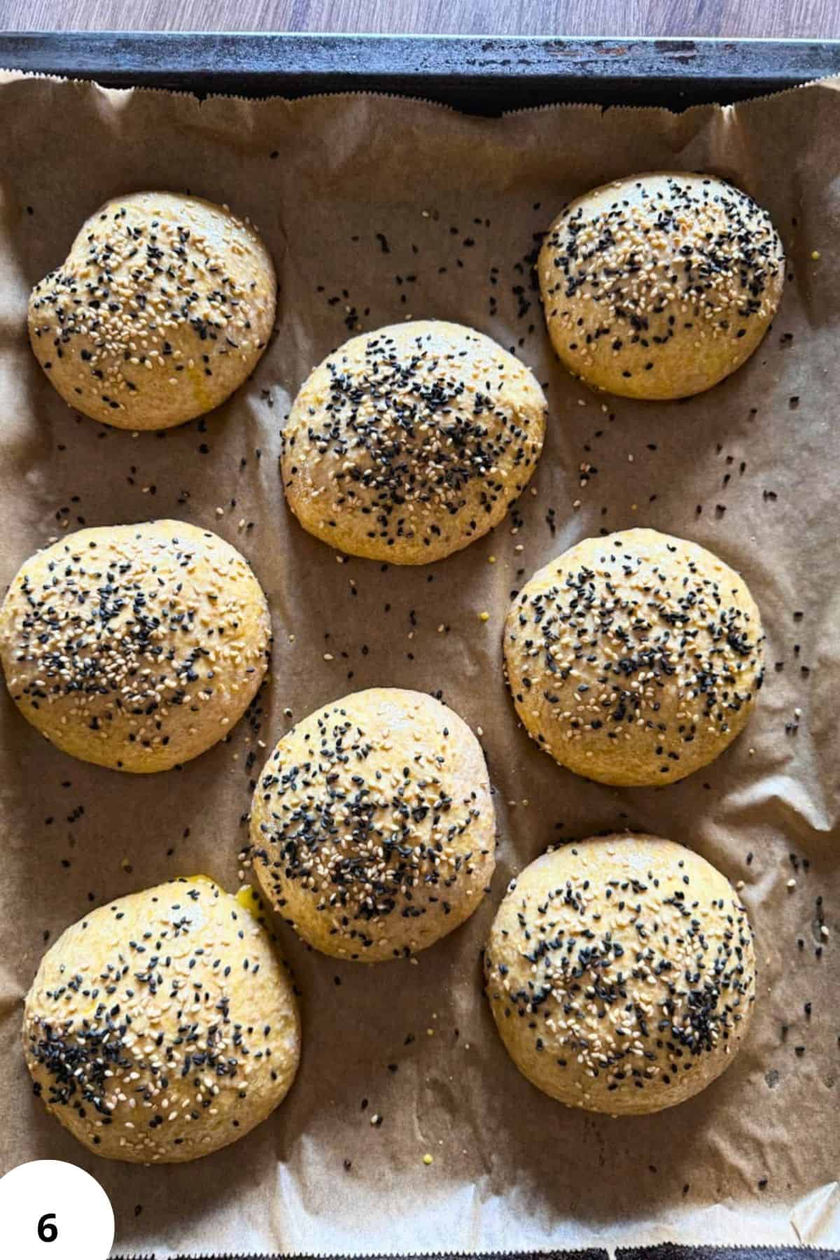 Freshly baked bread rolls topped with poppy seeds on baking sheet.