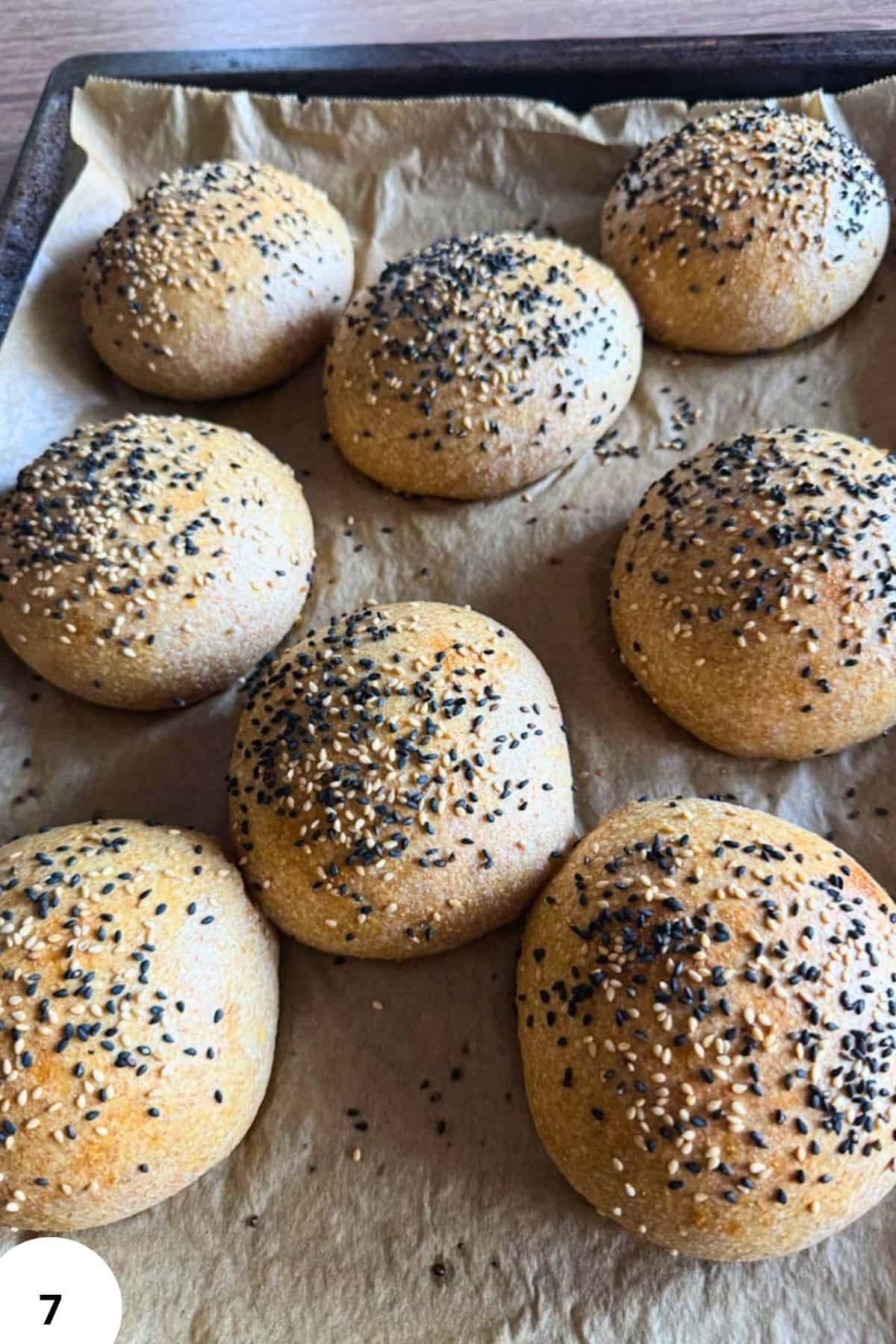 Freshly baked bread rolls topped with sesame and poppy seeds on baking sheet.