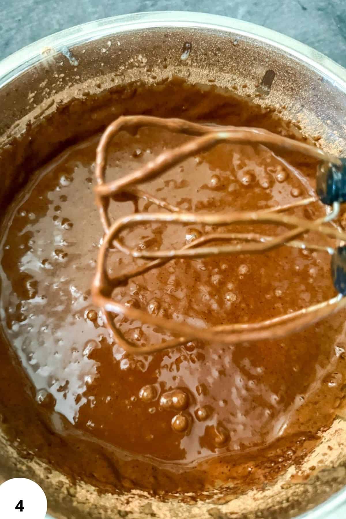 Chocolate dough being mixed with a hand mixer in a bowl.