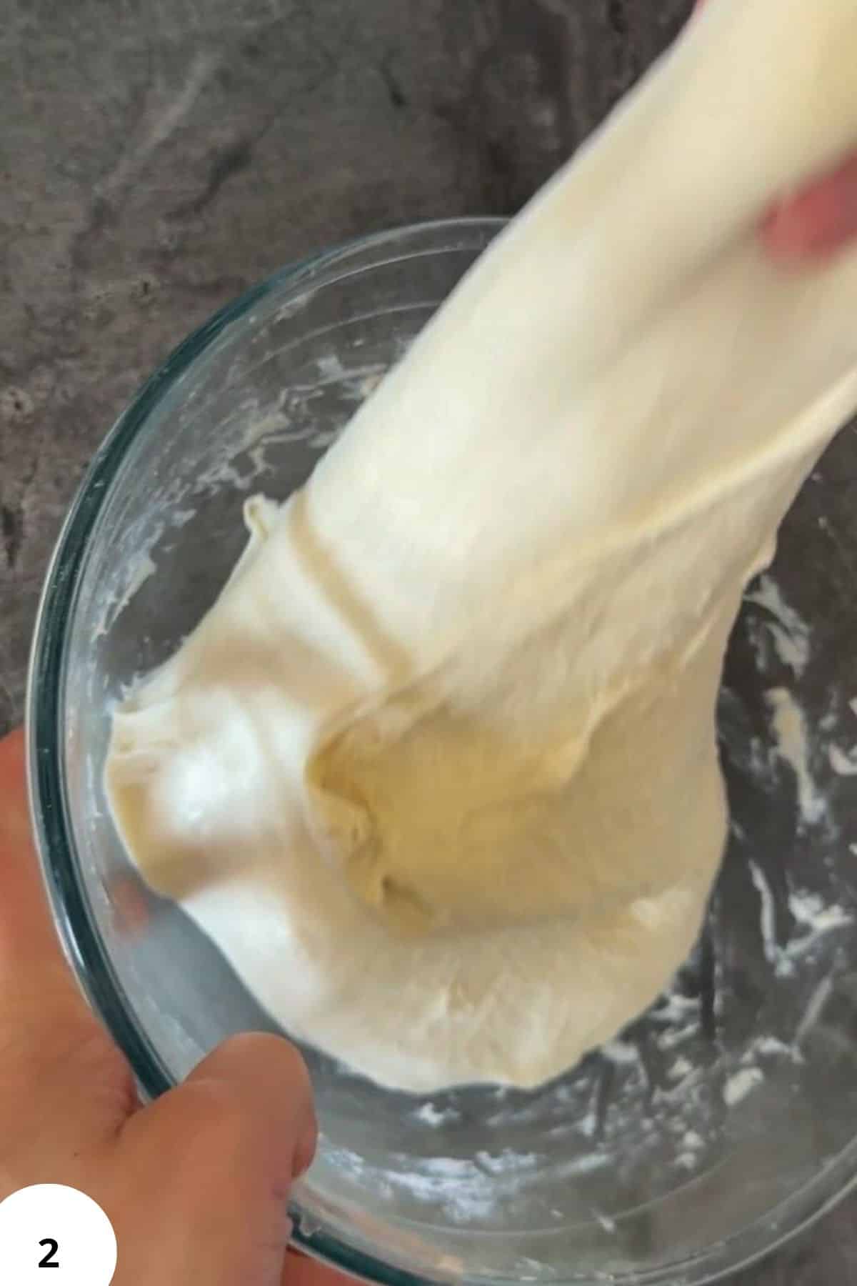 Stretch and fold dough technique for bread baking, close-up of dough being stretched in a glass bowl.