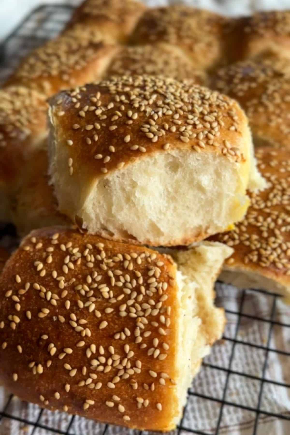 Freshly baked bread rolls topped with sesame seeds on a cooling rack.