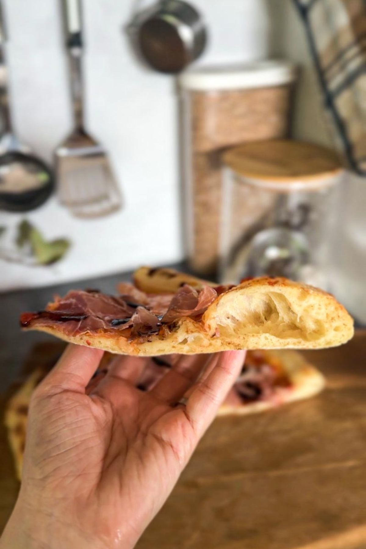 Close-up of a sourdough pizza slice with toppings in a cozy kitchen.