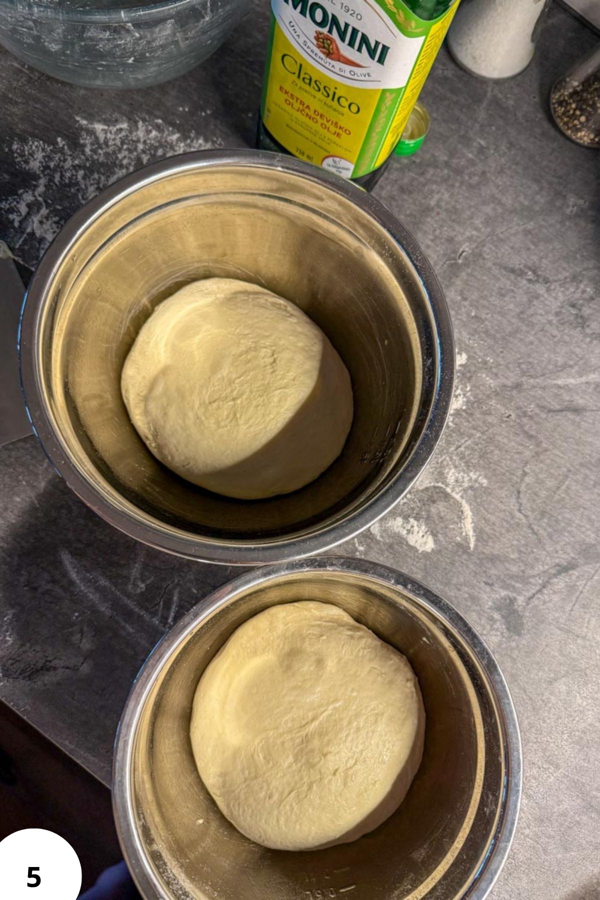 Two bowls of sourdough pizza dough rising in metal bowls.