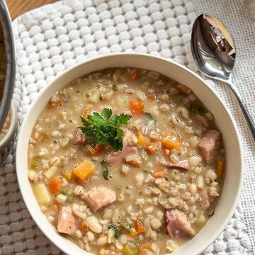Hearty barley and bean stew with smoked meat and vegetables in a bowl.