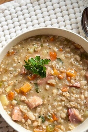 Hearty barley and bean stew with smoked meat and vegetables in a bowl.