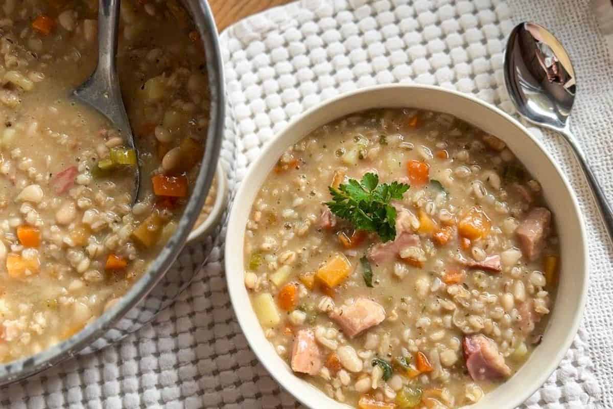 Hearty barley and bean stew with smoked meat and vegetables in a bowl.