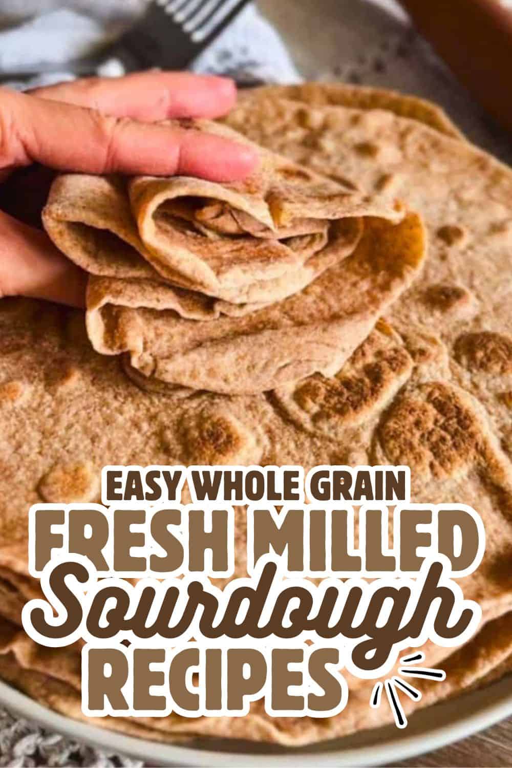 Hand holding freshly baked whole grain sourdough bread with a rustic appearance.