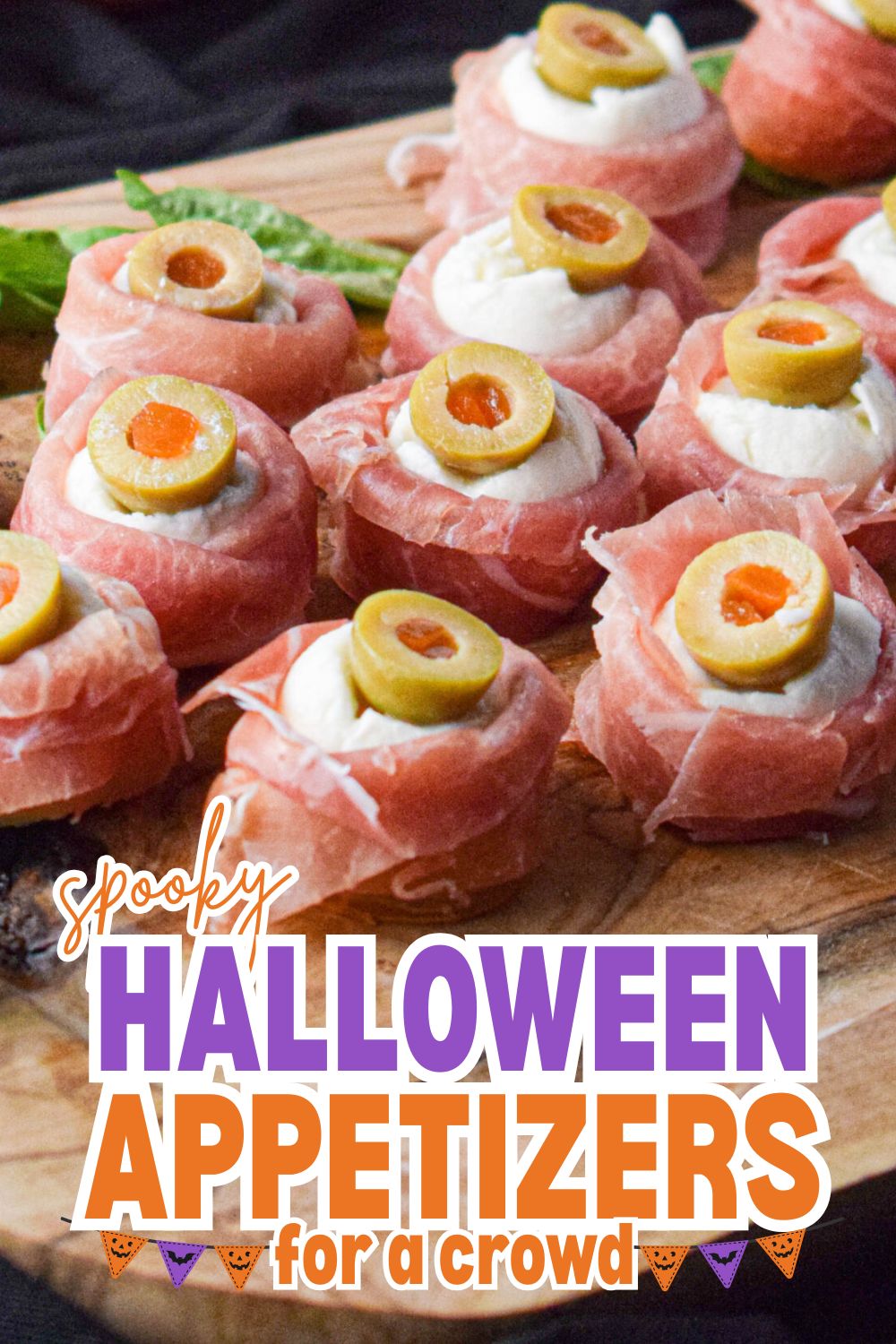 Spooky Halloween appetizers with olives, cheese, and prosciutto on a wooden board.