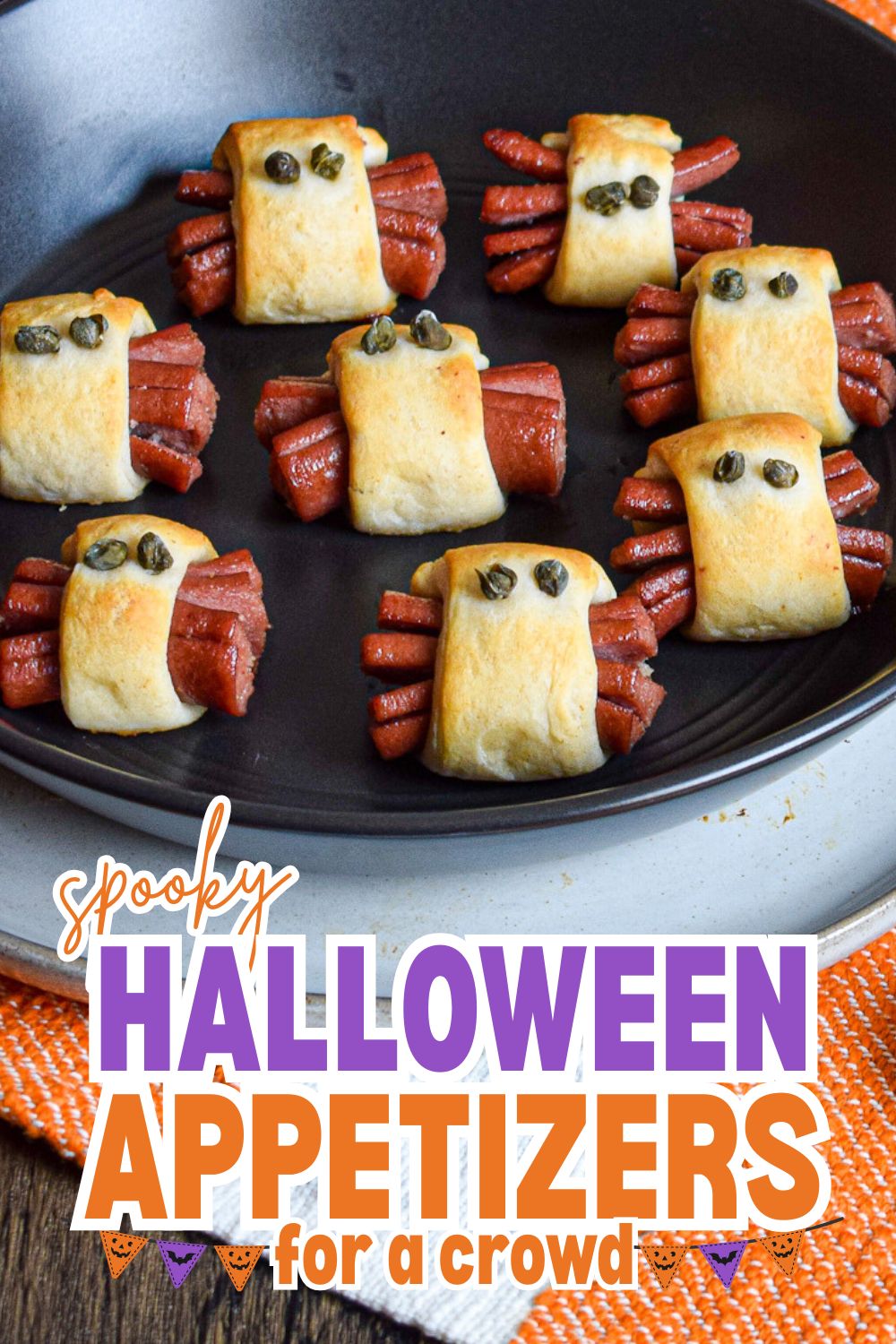 Spooky Halloween appetizers made with hot dogs wrapped in pastry with olive eyes.
