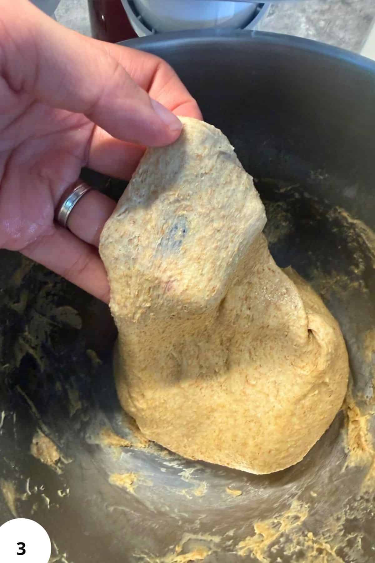 Hand folding dough in a mixing bowl for bread baking.
