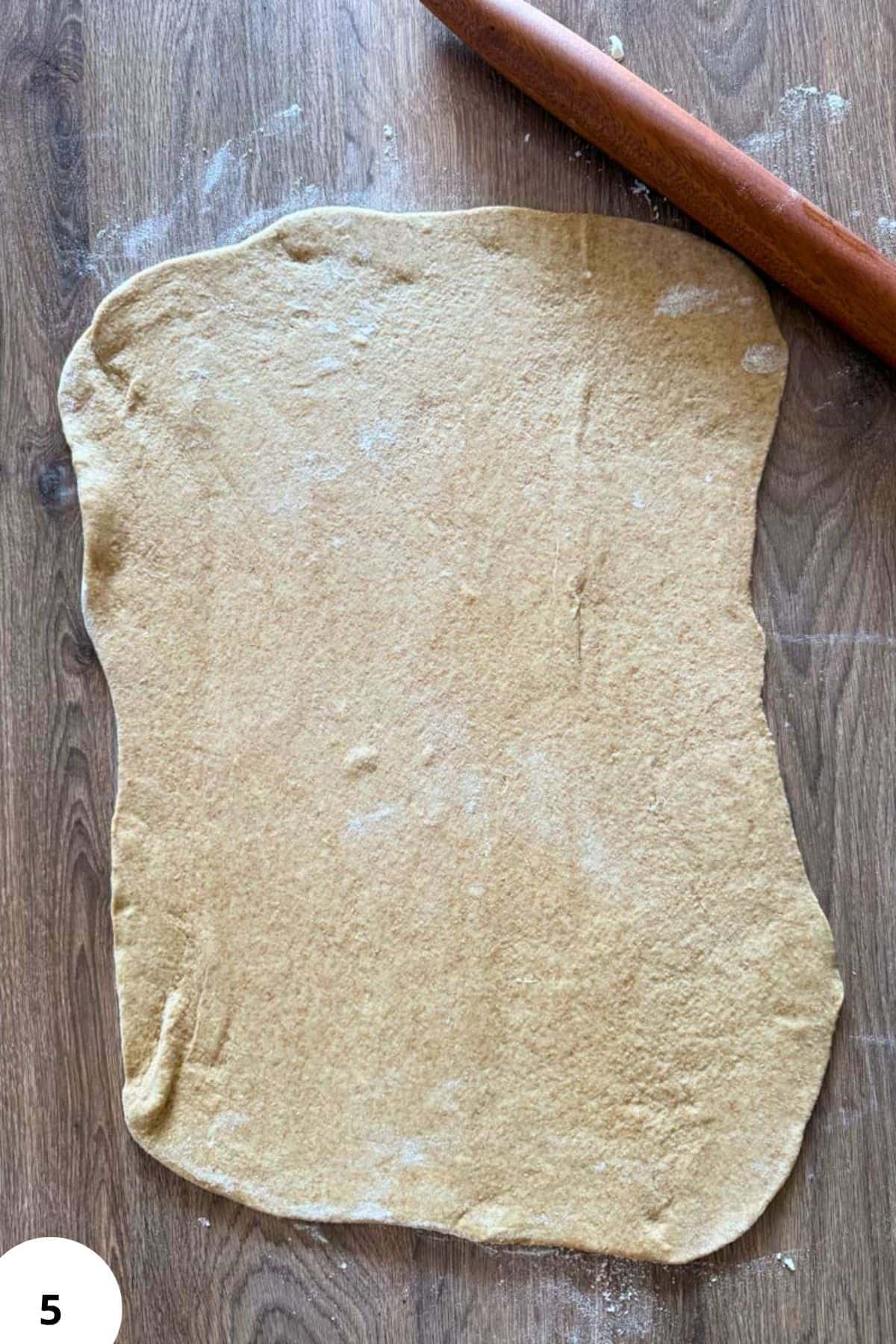 Rolling out dough with a rolling pin on a wooden surface for baking.