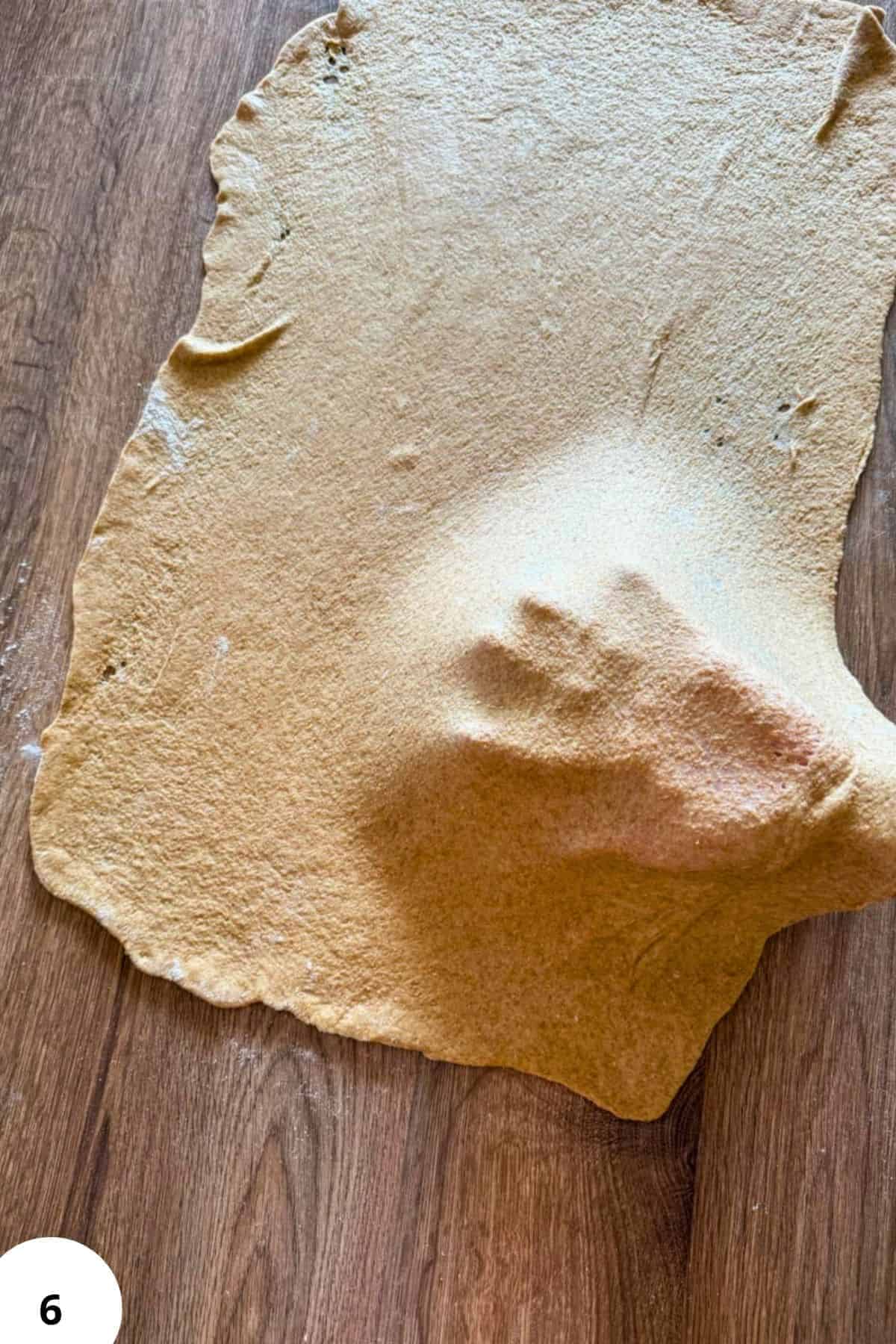 Unrolled dough for baking with a dusting of flour on a wooden surface.