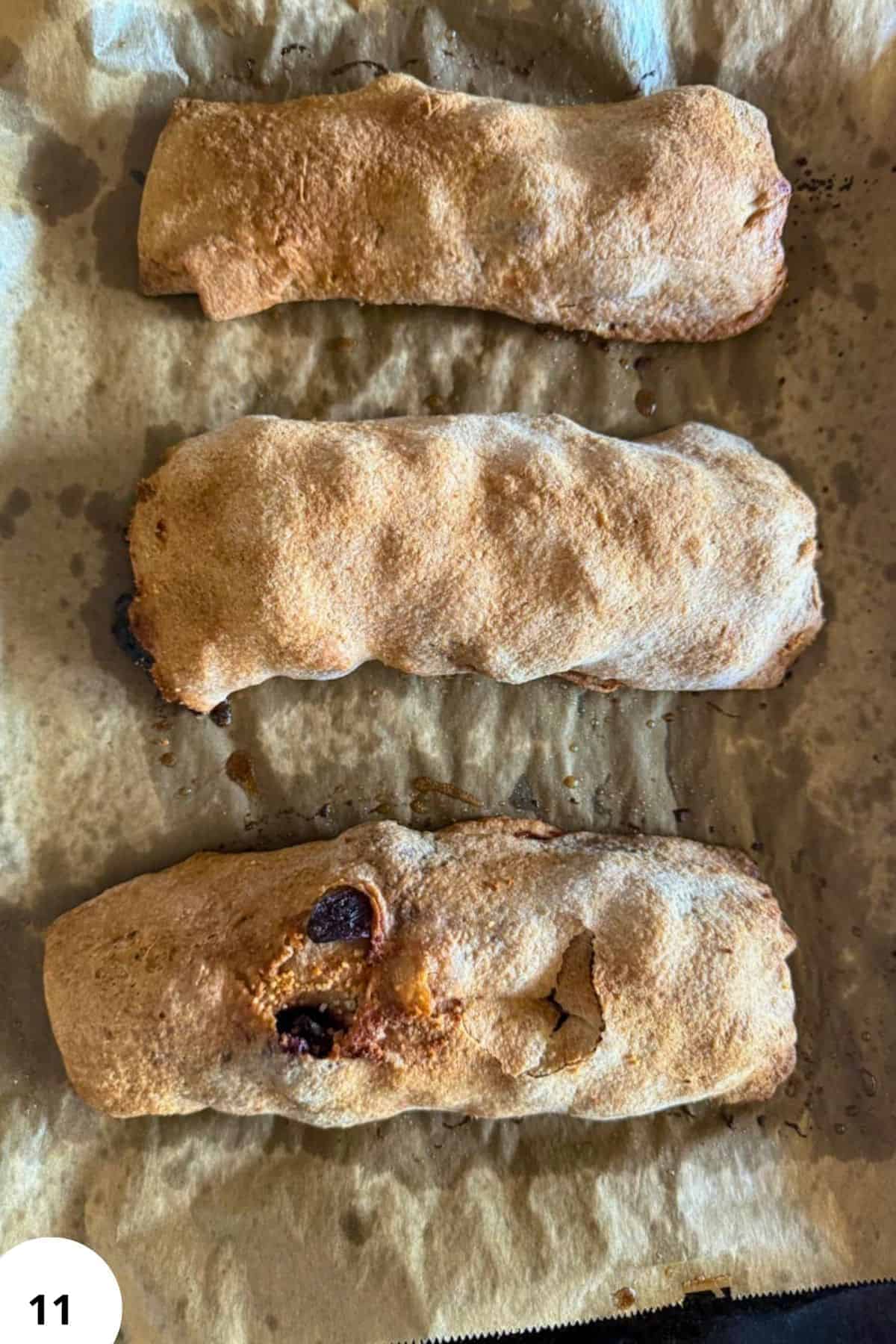 Three freshly baked cherry strudel pastries on parchment paper.