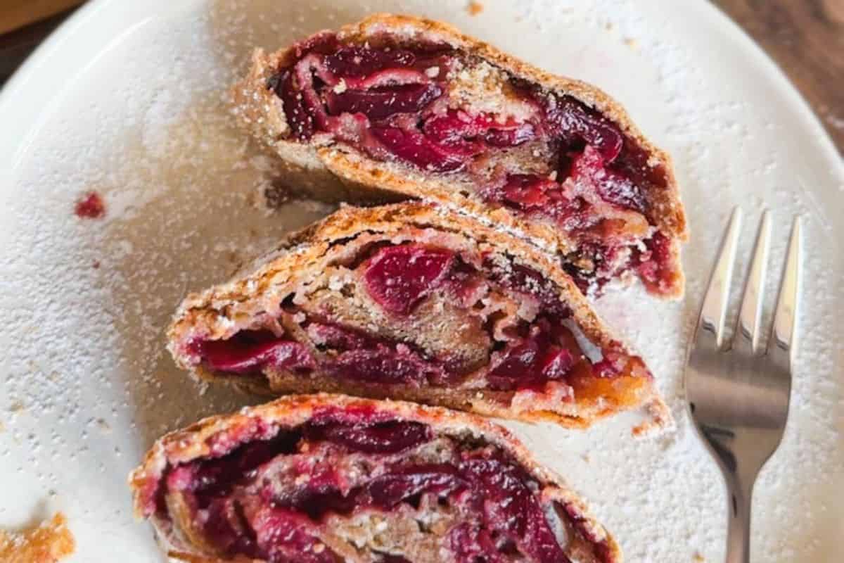 Close-up of cherry-filled strudel with powdered sugar on a white plate.