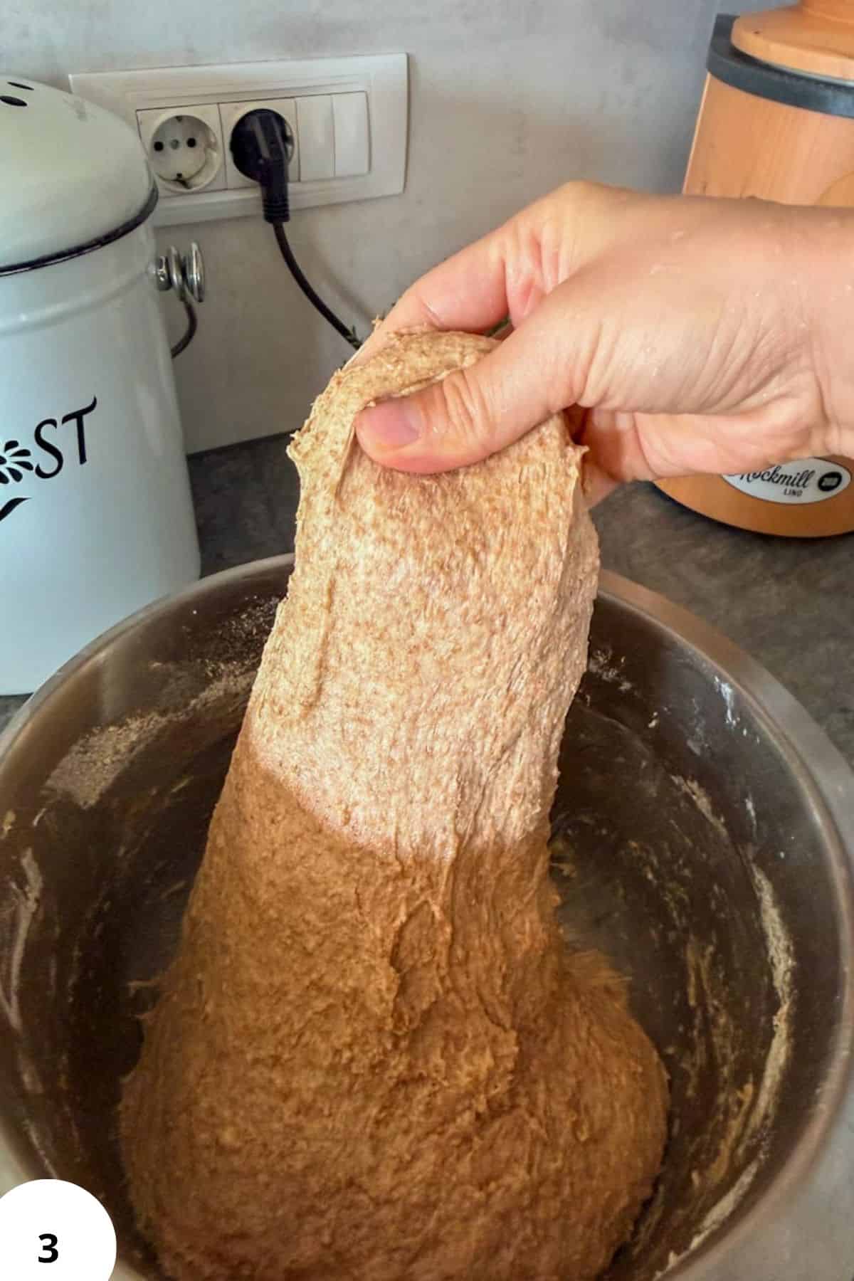 Person handling freshly milled sourdough dough in a mixing bowl.