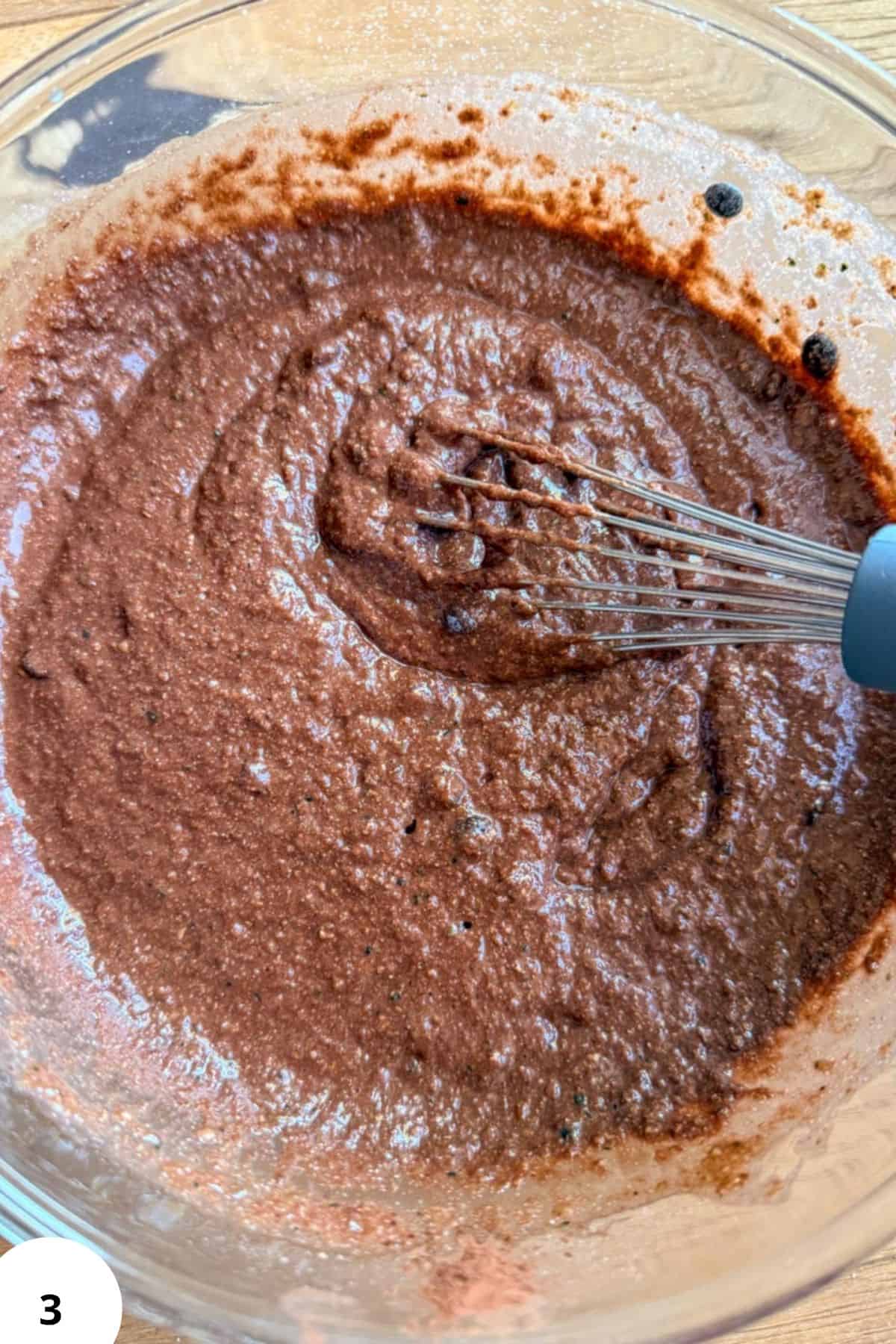 Chocolate zucchini muffin batter in a glass bowl with whisk.