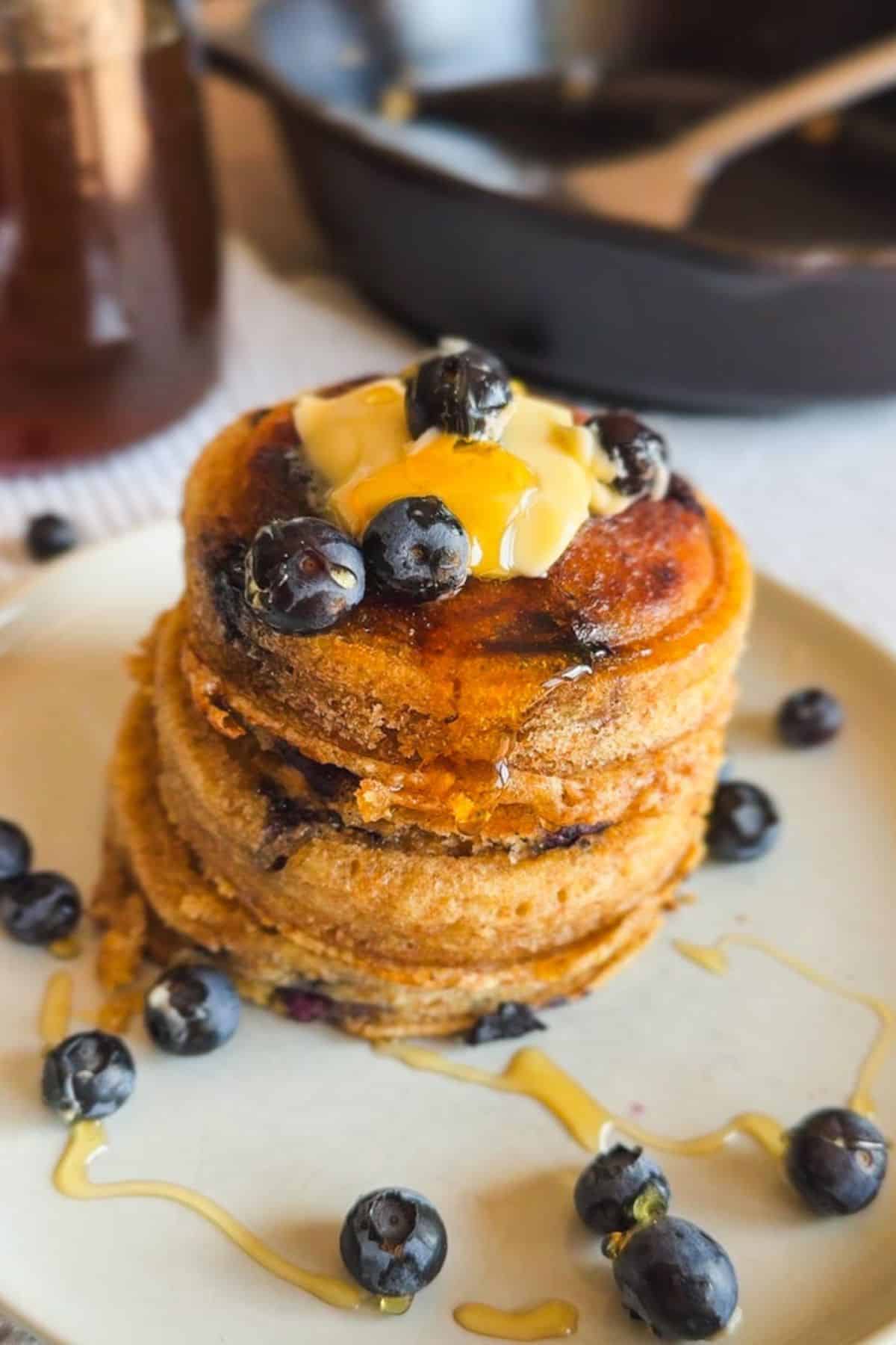 Stack of blueberry pancakes with syrup and fresh blueberries on a plate.