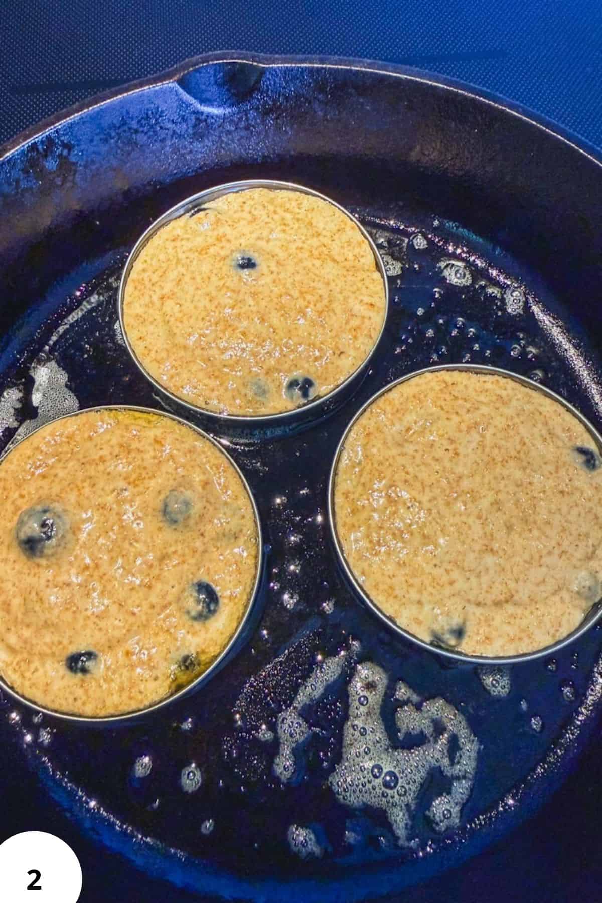 Cooking sourdough pancakes in a skillet with blueberries and butter.