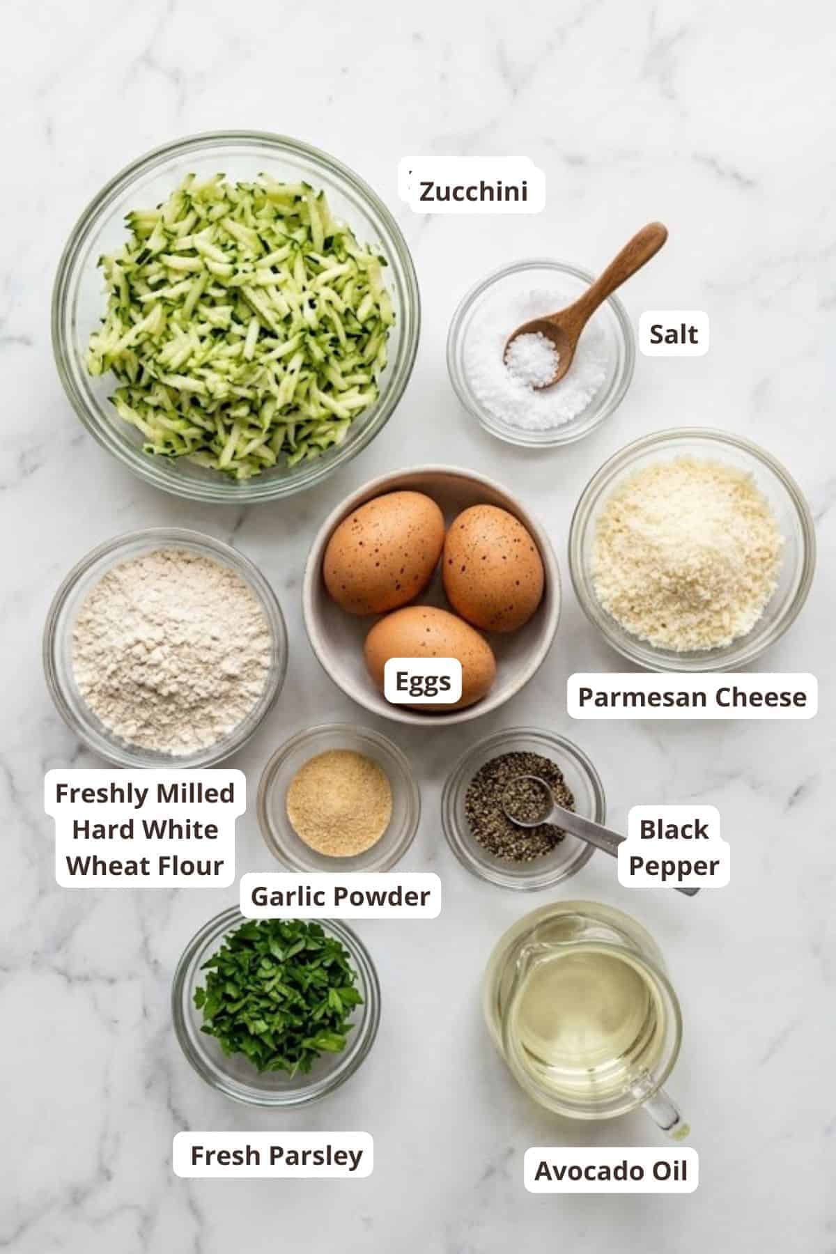 Ingredients for zucchini fritters including zucchini, eggs, cheese, and herbs.