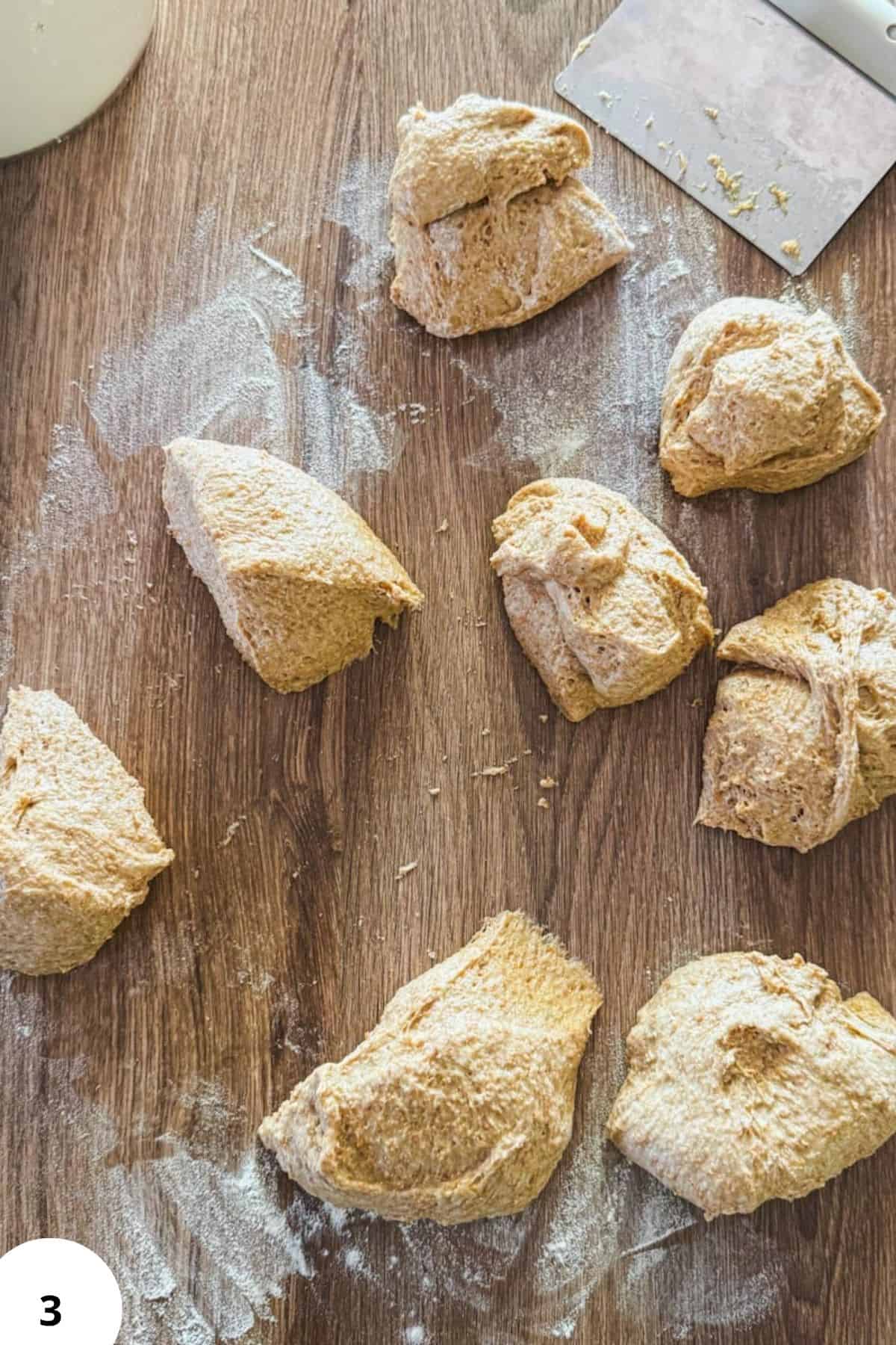 Freshly prepared sourdough hot dog buns on a wooden surface with flour and a dough scraper.