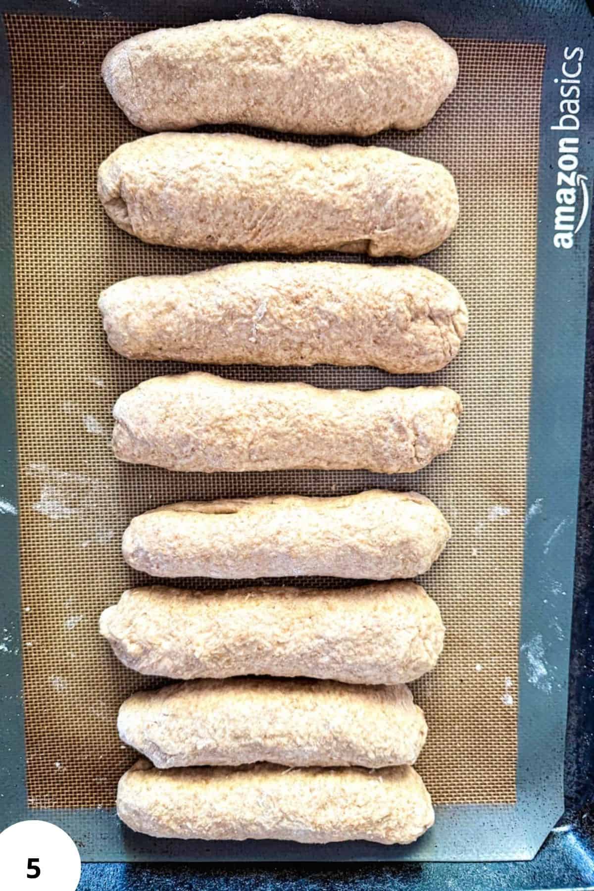 Freshly shaped sourdough hot dog buns on a baking sheet.