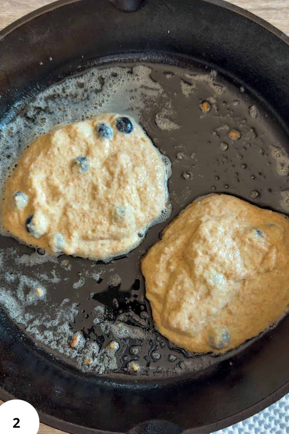 Cooking sourdough pancakes in a skillet with blueberries and batter.