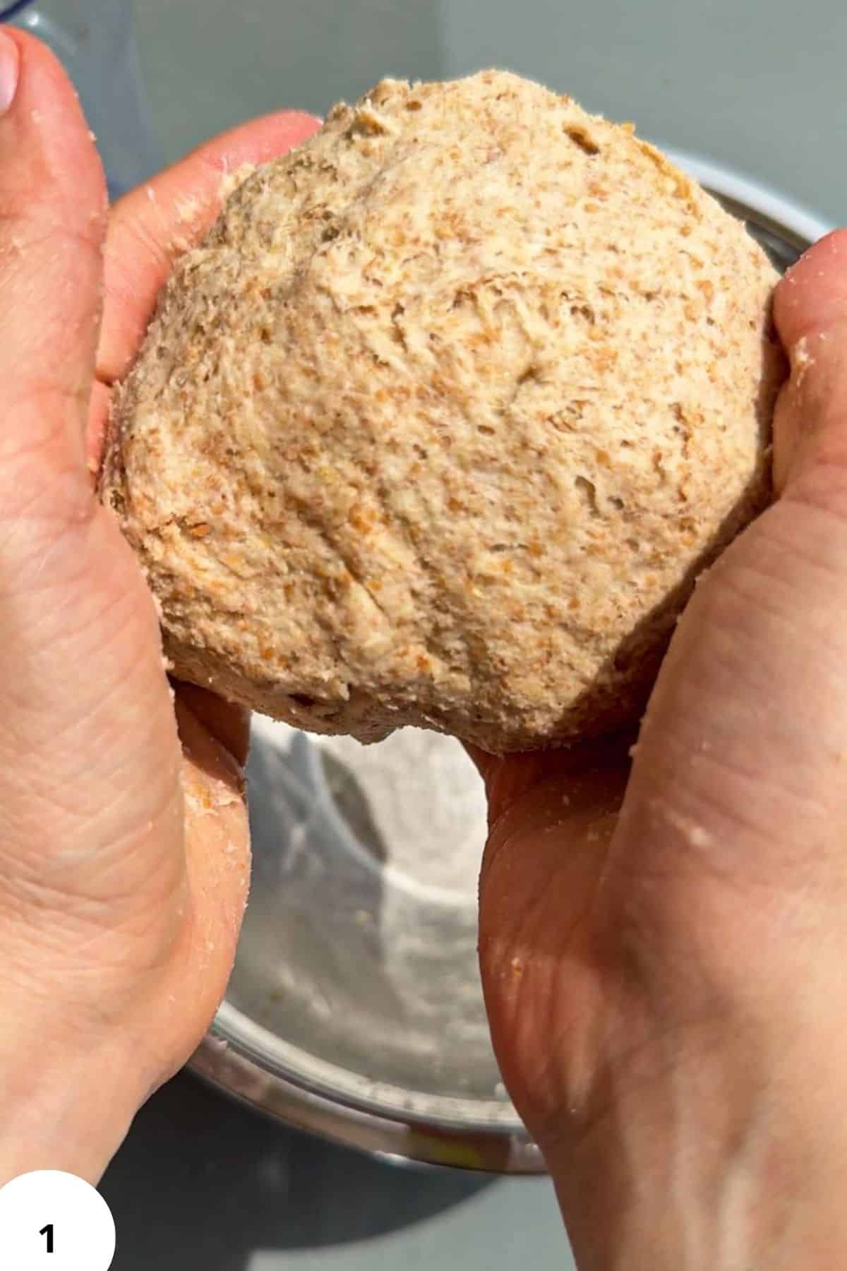 Close-up of a hand holding a freshly baked sourdough seed cracker.