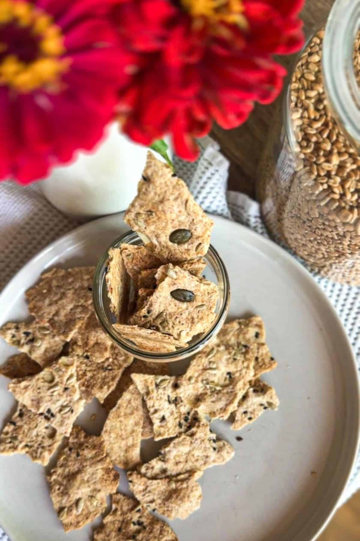 Homemade sourdough seed crackers served on a white plate with flowers and grains in the background.