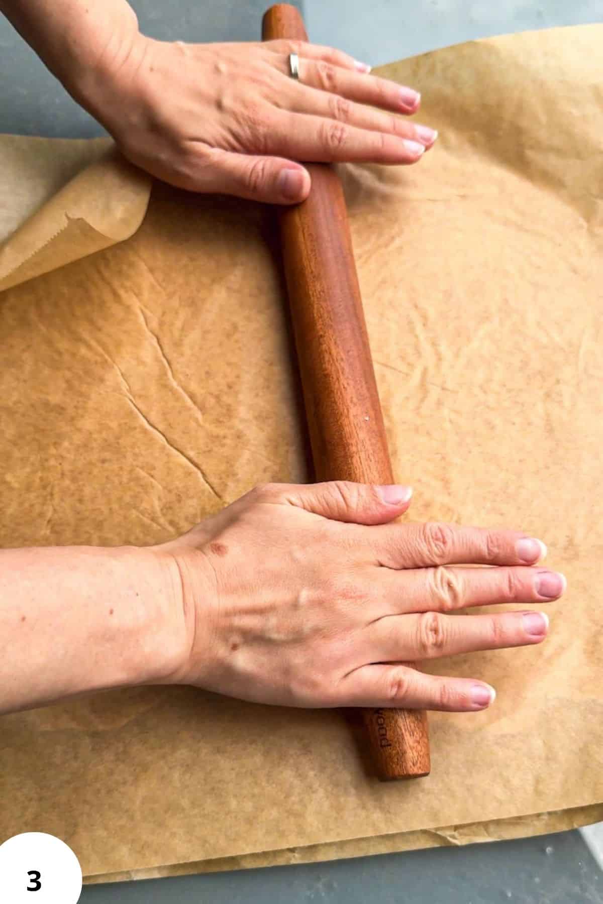 Person rolling sourdough cracker dough with a wooden rolling pin.