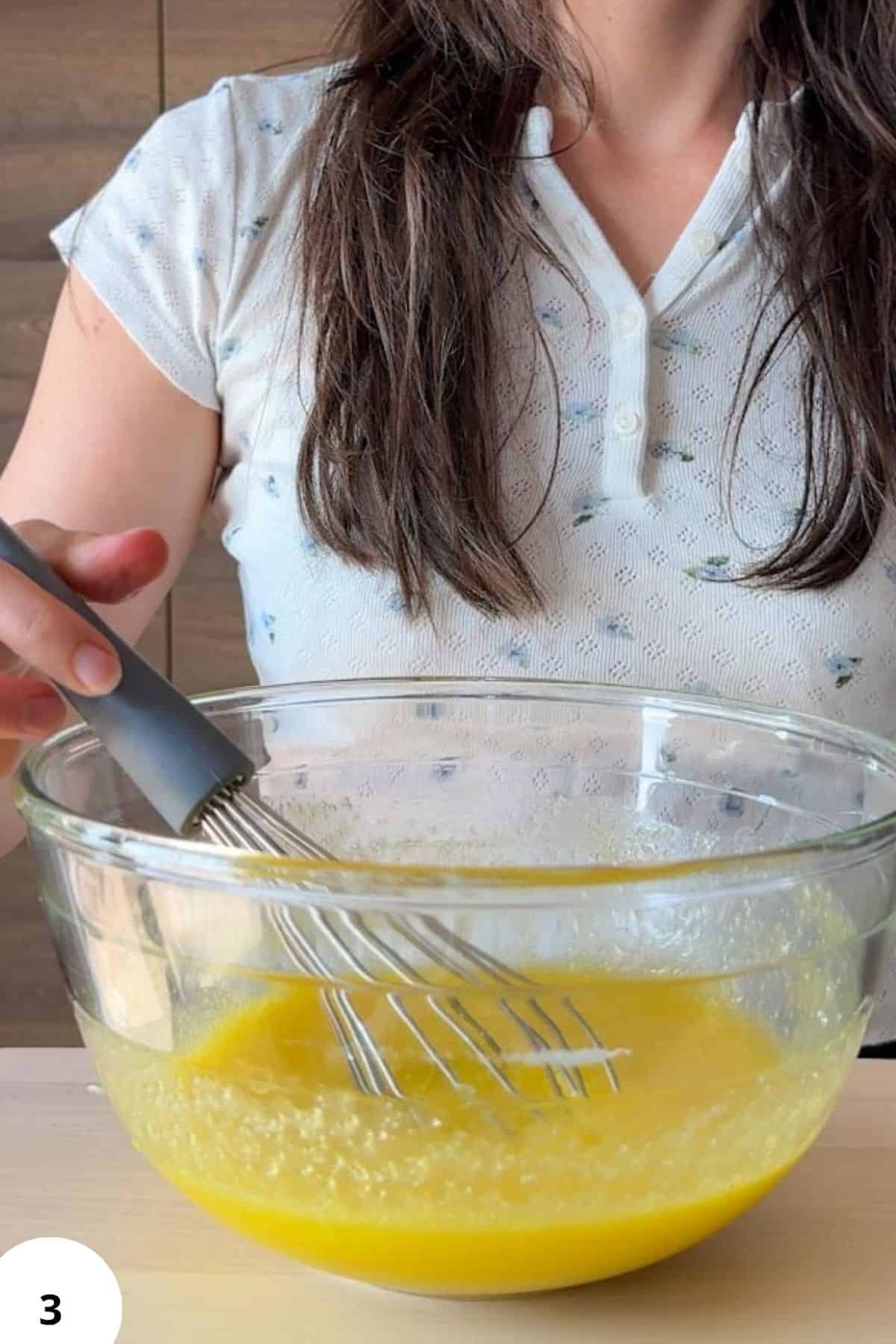 Person whisking zucchini bread batter in a glass bowl with a hand mixer.