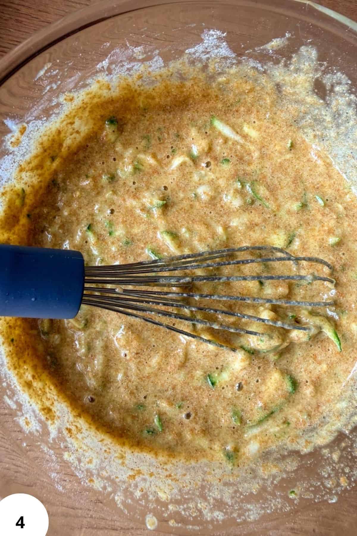 Mixing zucchini bread batter with a whisk in a glass bowl.