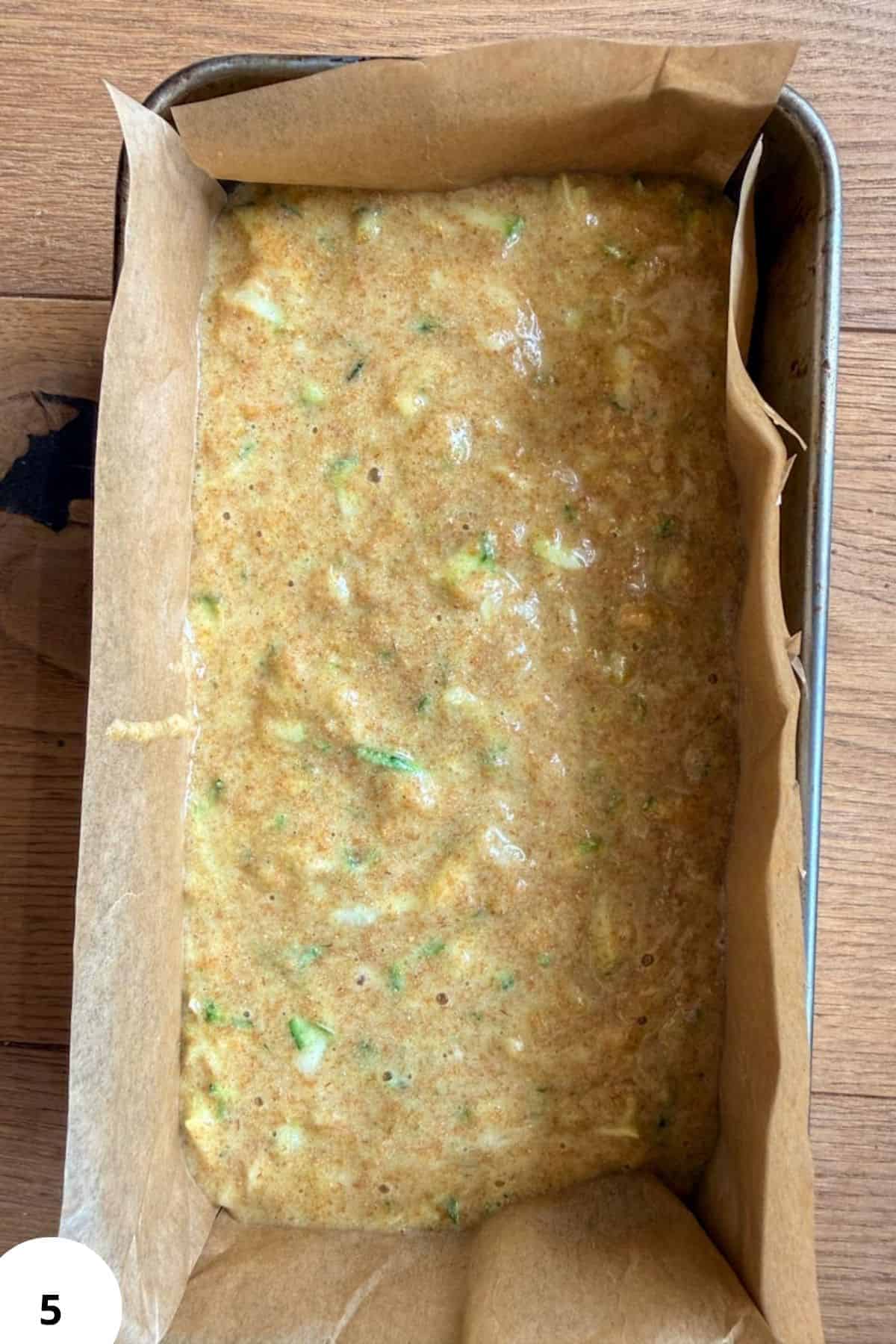 Raw zucchini bread batter in a baking pan with parchment paper.
