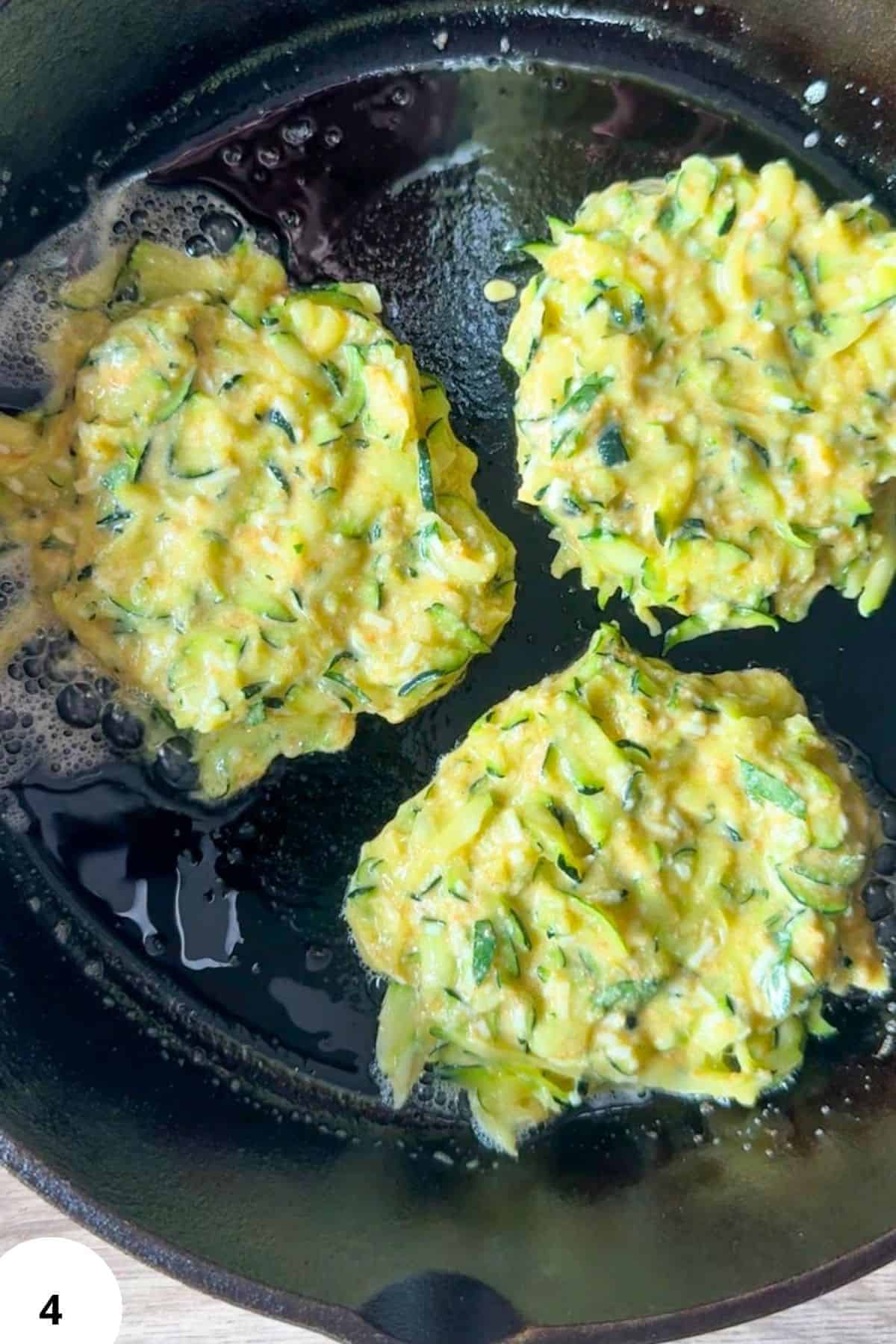 Zucchini fritters frying in a skillet with oil.