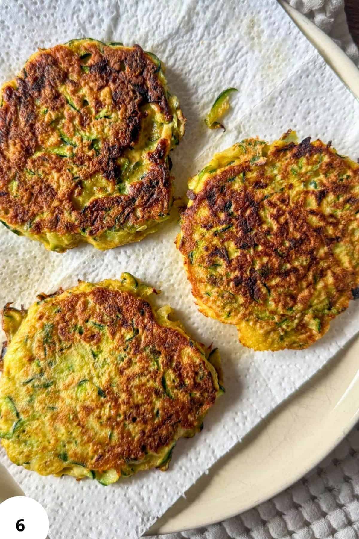 Golden zucchini fritters on a white plate with a knife.