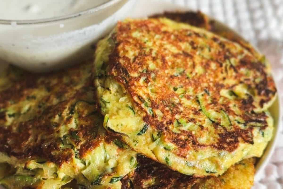 Close-up of crispy zucchini fritters with herbs on a plate.