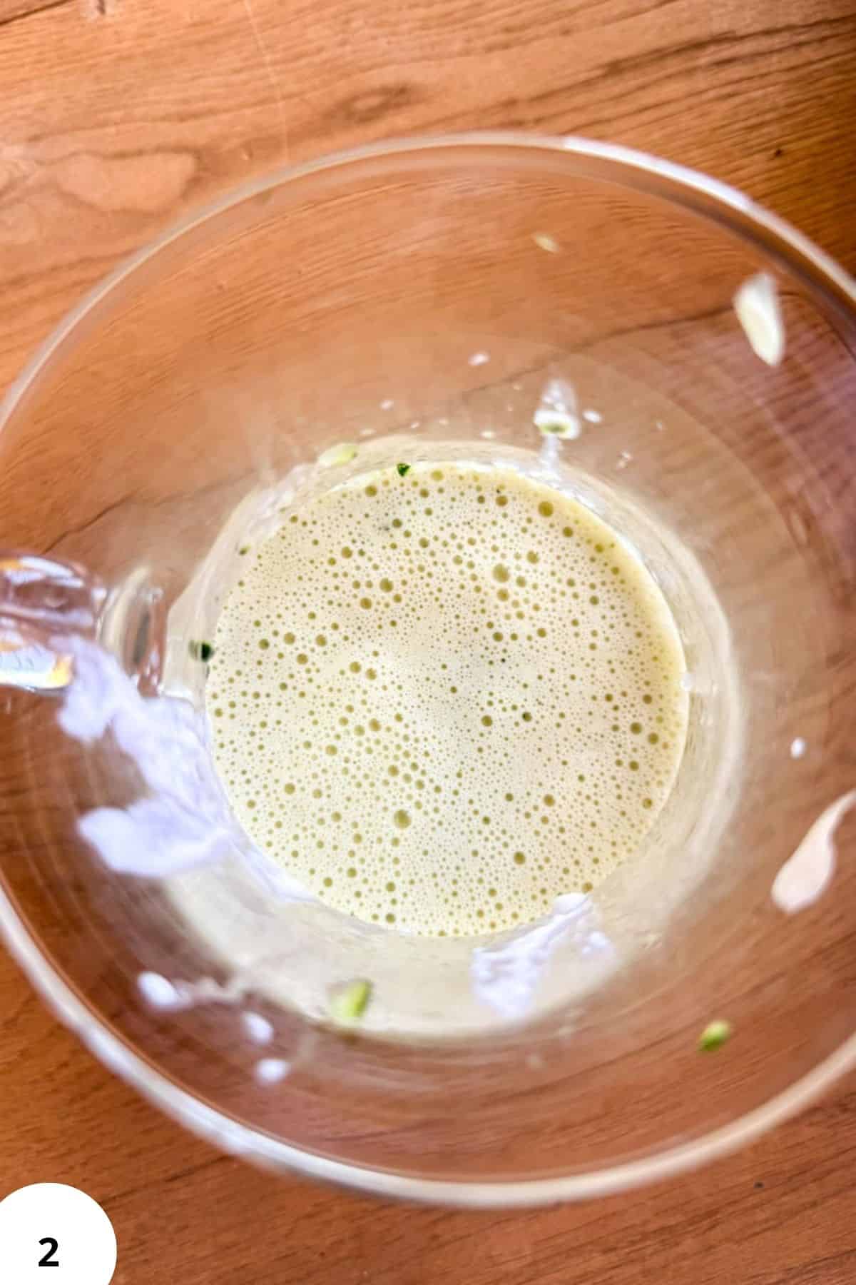 Frothy sourdough starter with zucchini bits in a glass bowl on wooden surface.