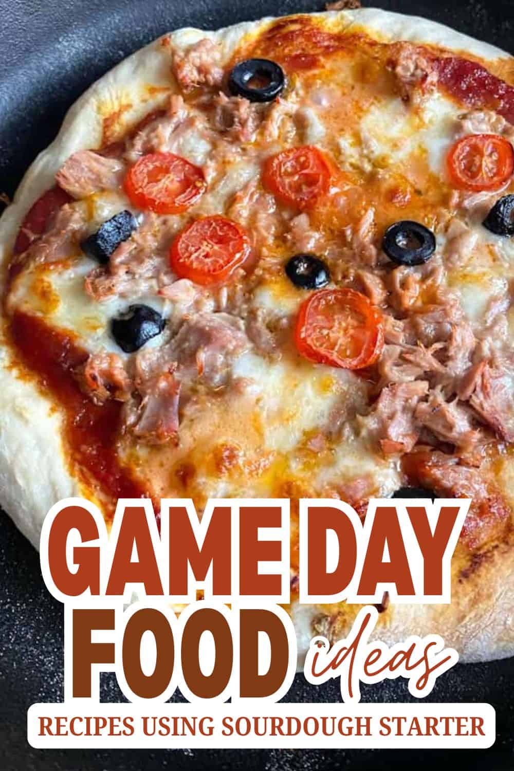 Close-up of homemade pizza topped with cherry tomatoes, black olives, tuna, and melted cheese.