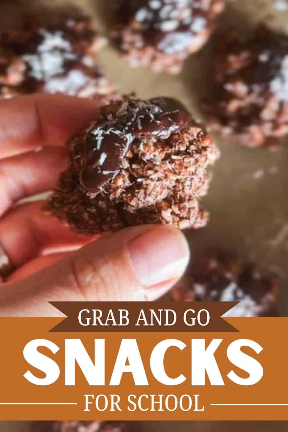 Chocolate snack held in hand with blurred snacks in background.