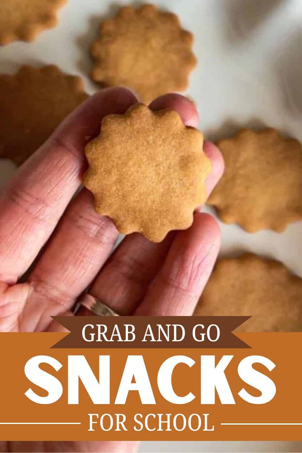 Hand holding a round cookie with other cookies in the background.