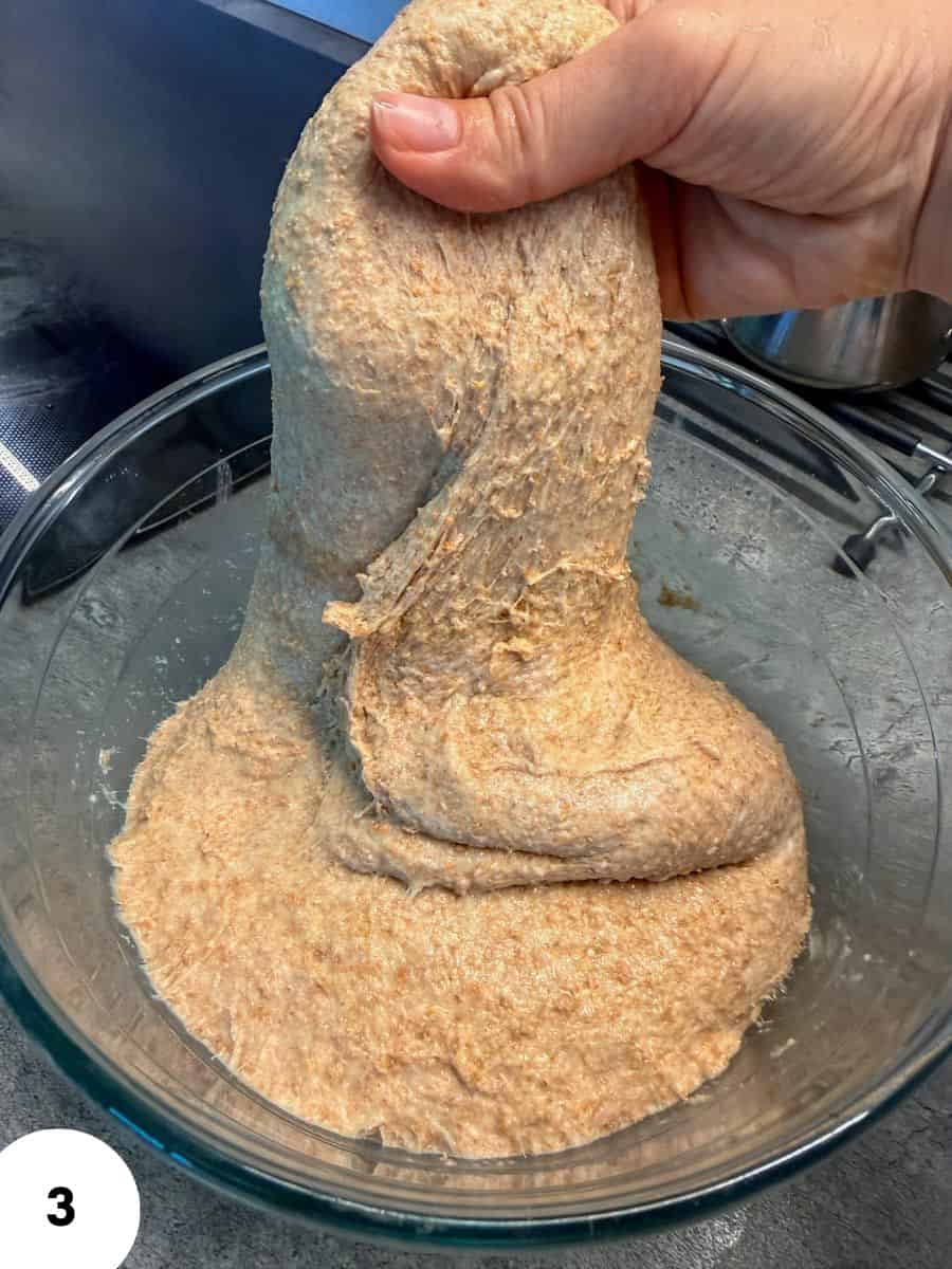 Hand performing stretch and fold dough technique for bread fermentation.