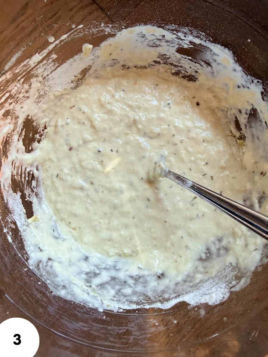 Creamy dough mixture for bread baking with a metal spoon.