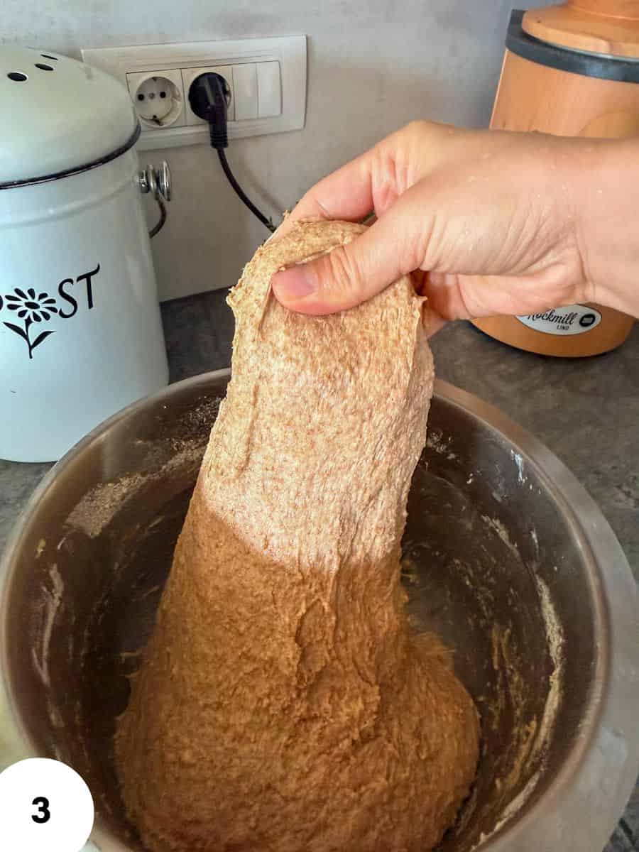 Person performing stretch and fold technique on bread dough in a bowl.