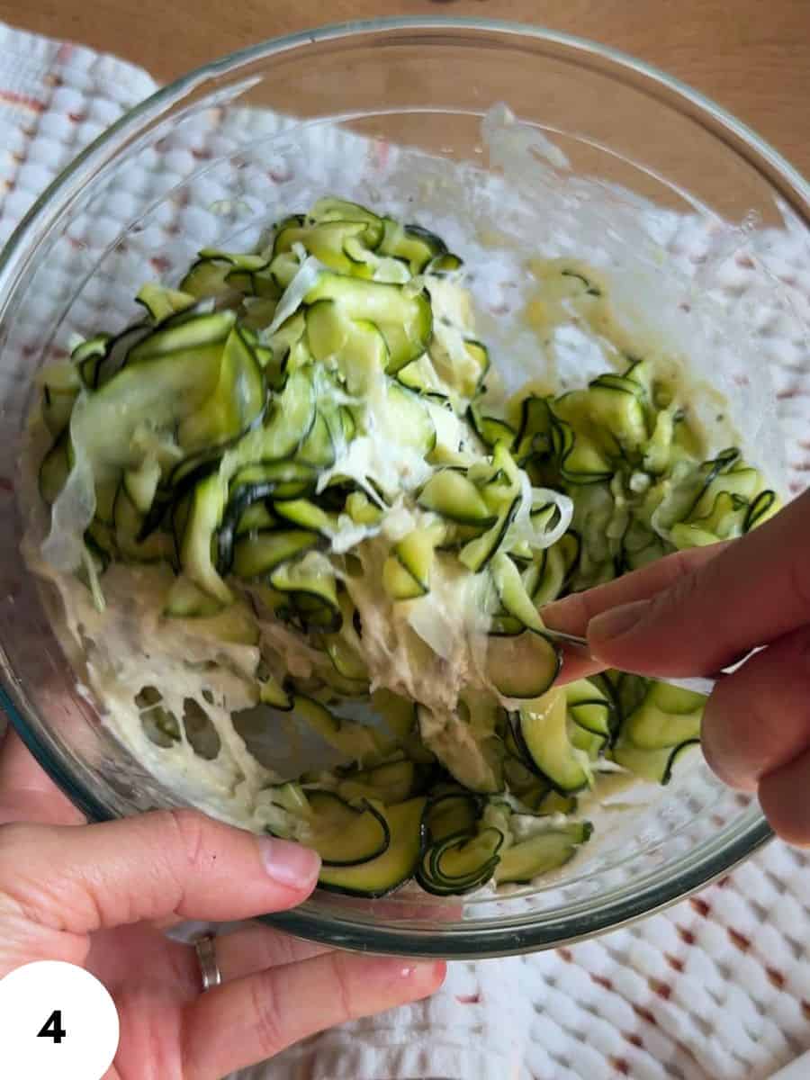Hands performing stretch and fold technique on dough with zucchini in a glass bowl.