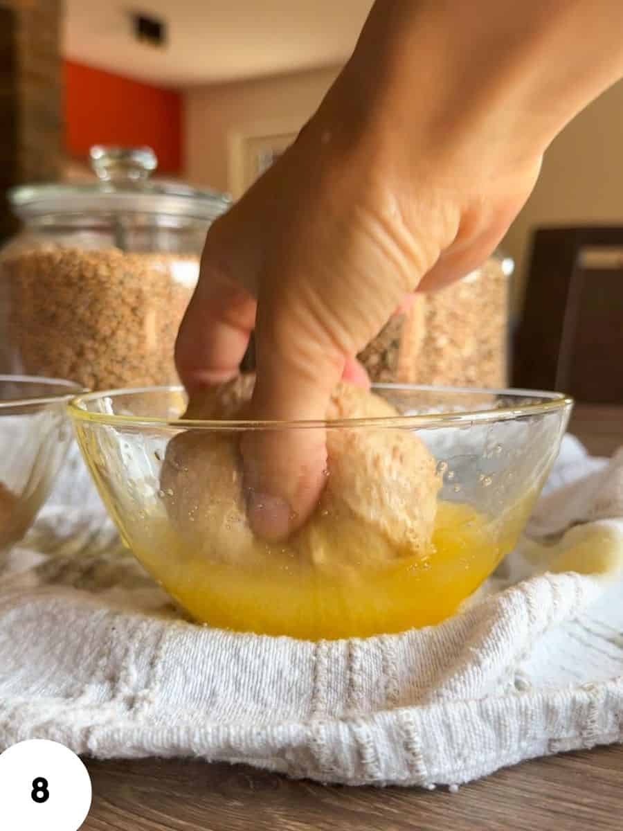 Hand performing stretch and fold dough in a glass bowl for bread making.