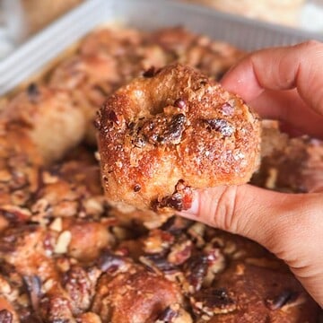 Close-up of a hand holding a sticky pecan pie pull-apart sourdough piece.